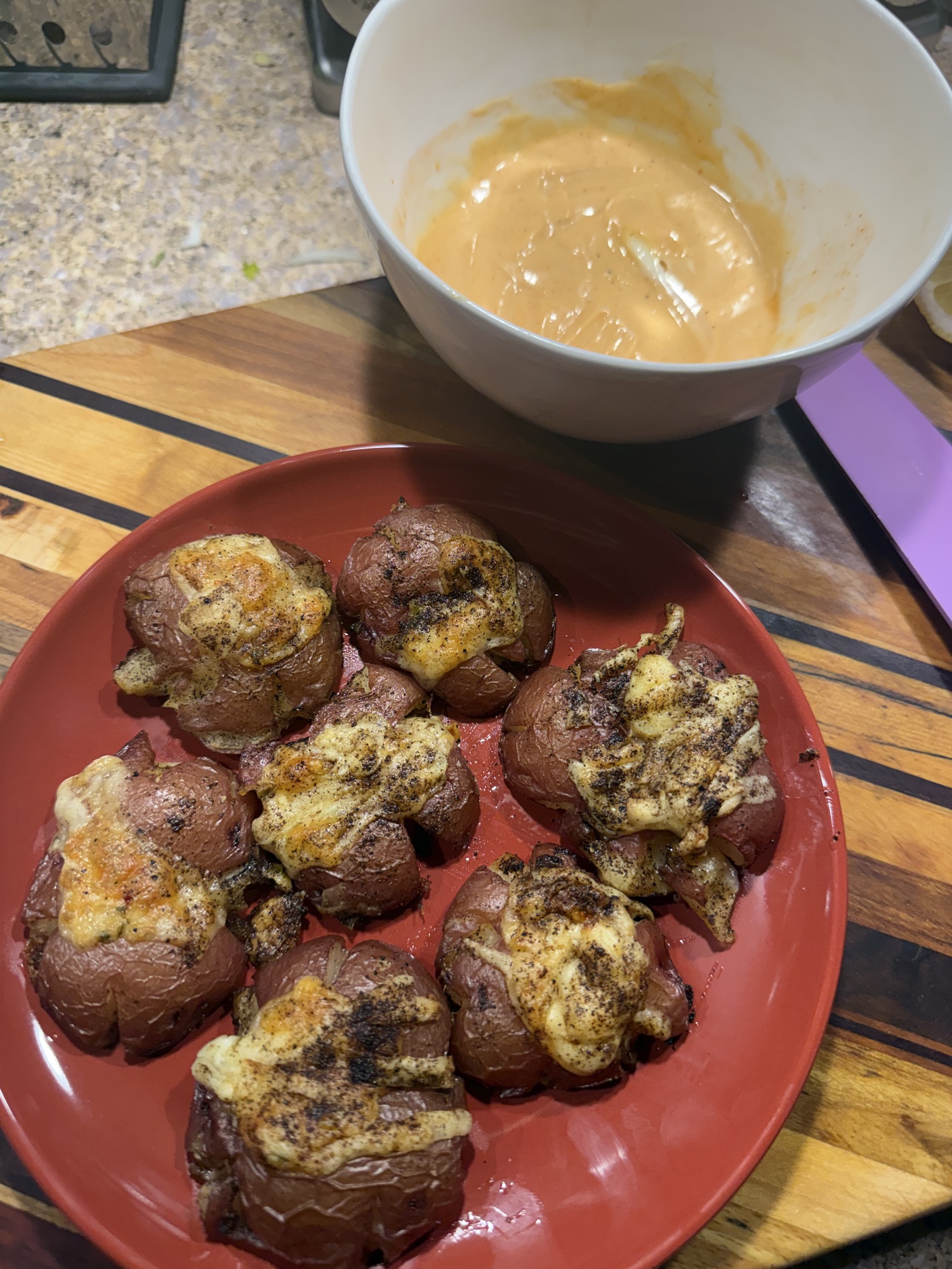 smashed baby reds with aged cheddar on a red plate, dipping sauce in the background